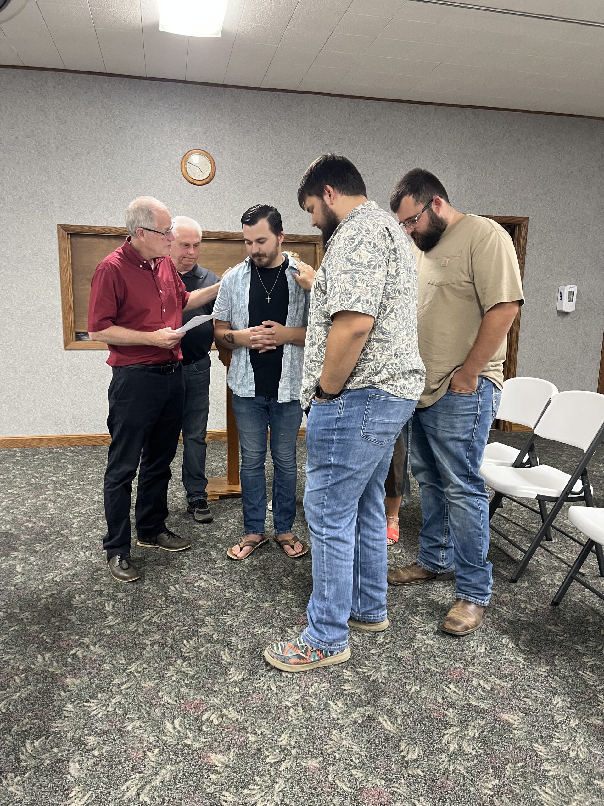 Members of New Life Fellowship standing in a circle with heads bowed, praying over one of their members.