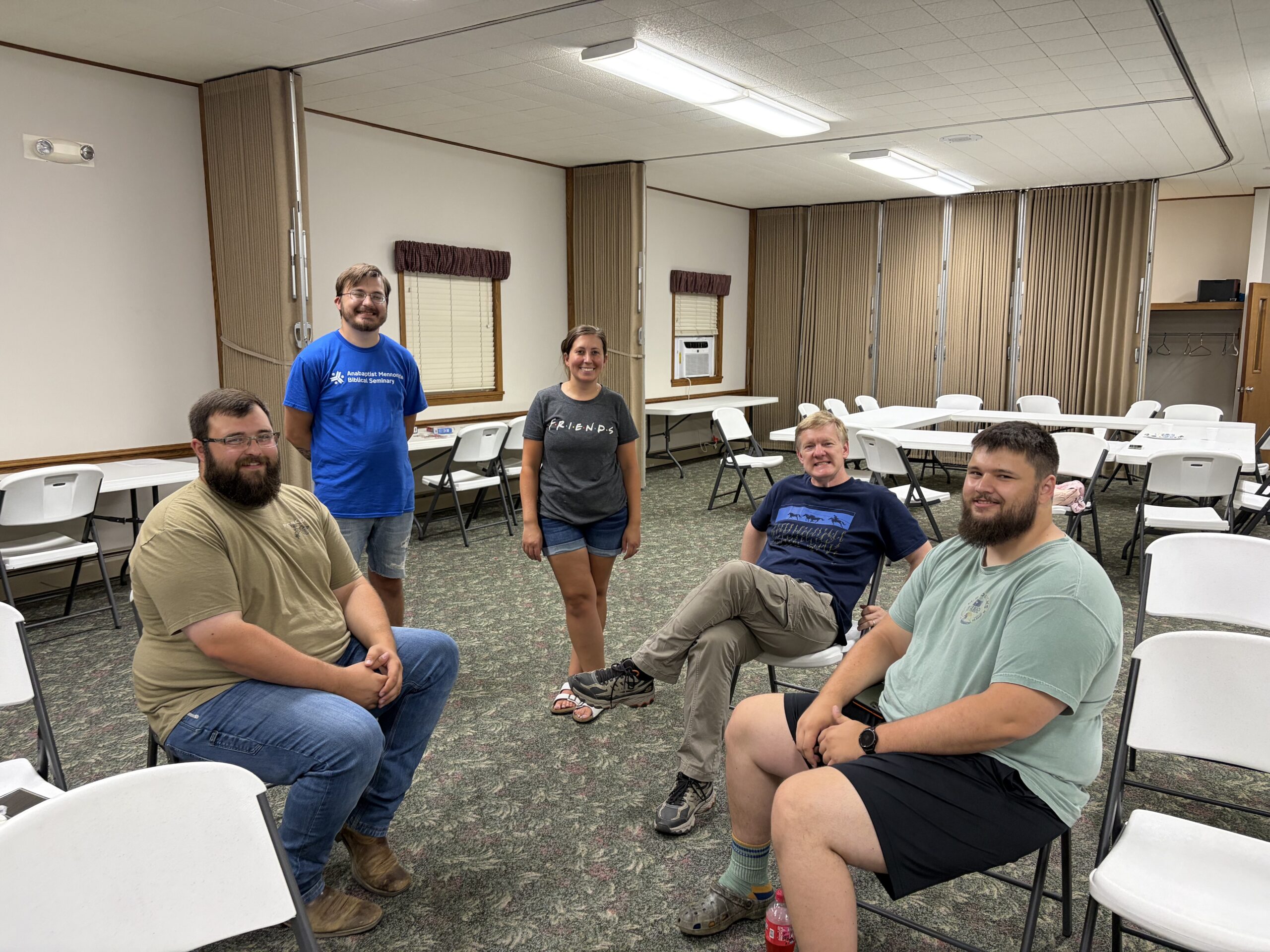 Members of New Life Fellowship sitting and standing together in the fellowship hall after a gathering, several in matching t-shirts.