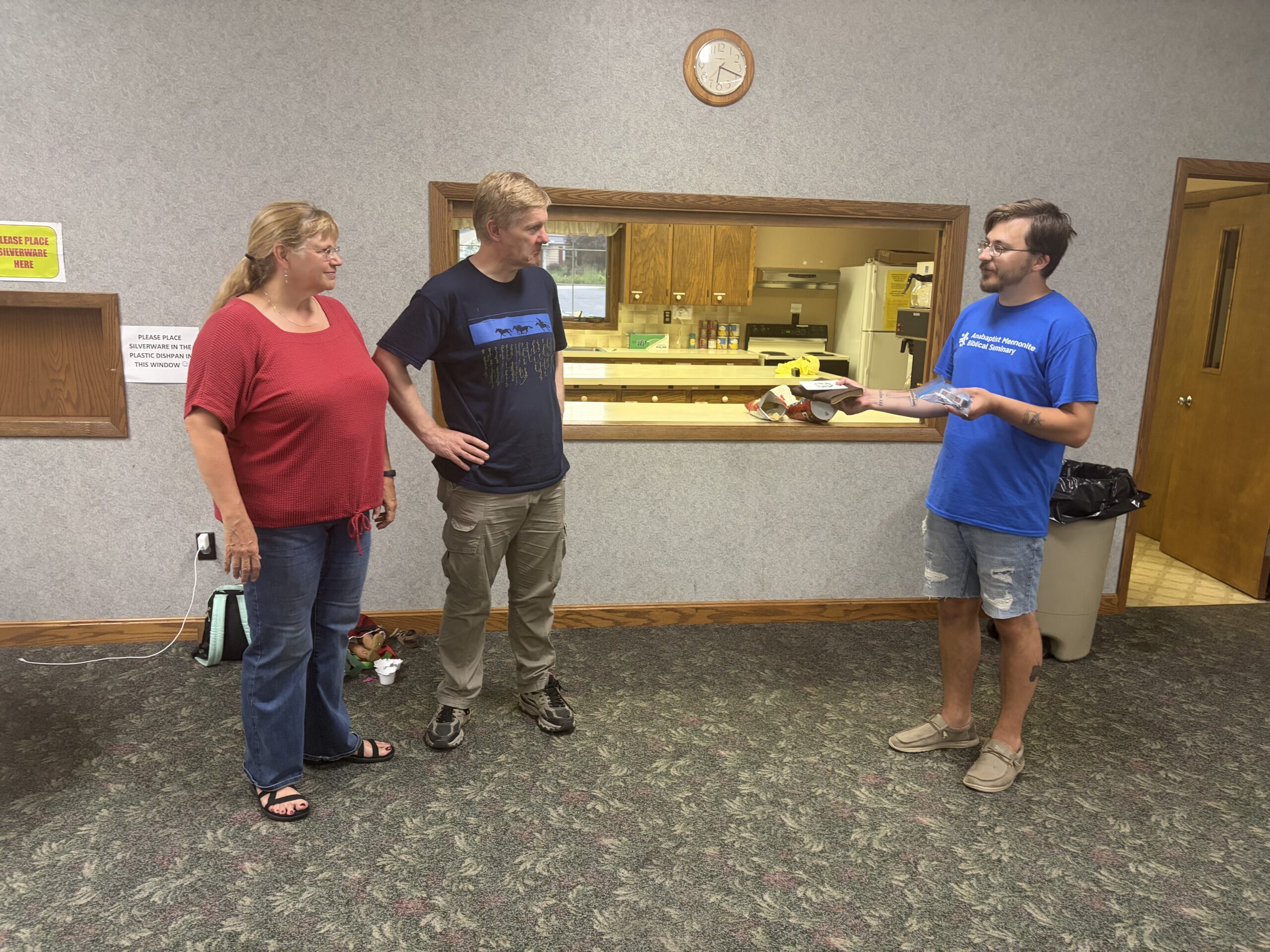 Three members of New Life Fellowship talking together beside the kitchen serving window.